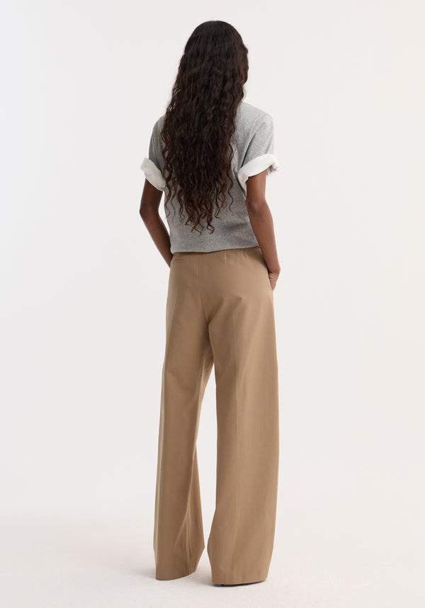 Back view of a person wearing Classic loose fit chino in beige, featuring a relaxed fit, high-waist, and side pockets. Hands in pockets, showcasing the tailored waistband.