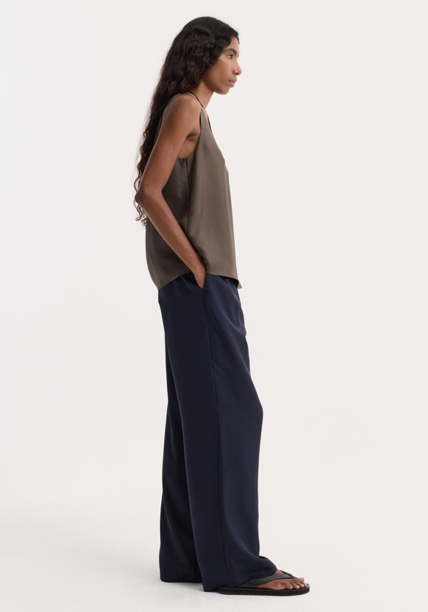 Woman in side profile wearing Relaxed silk trousers | night, featuring wide legs and an elasticated waistband, with hands in pockets and black sandals.