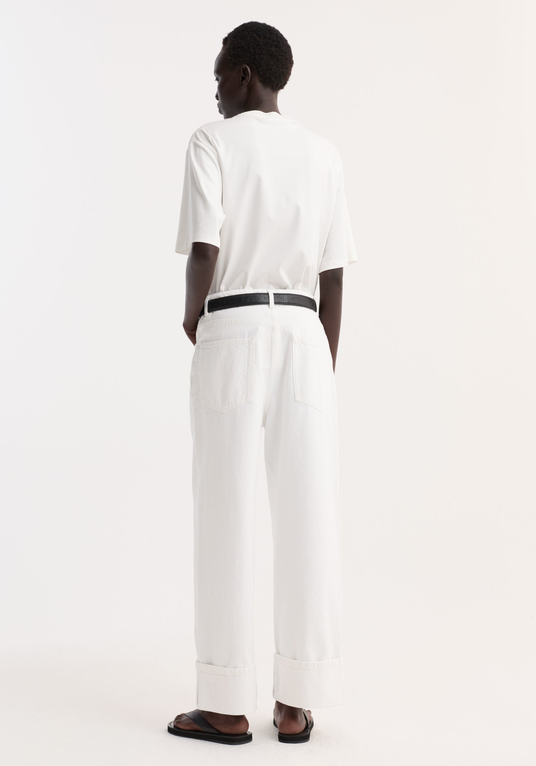 Person wearing Baggy fit turn-up denim in optic white, featuring a wide leg and low-rise, paired with a black belt and flat sandals.