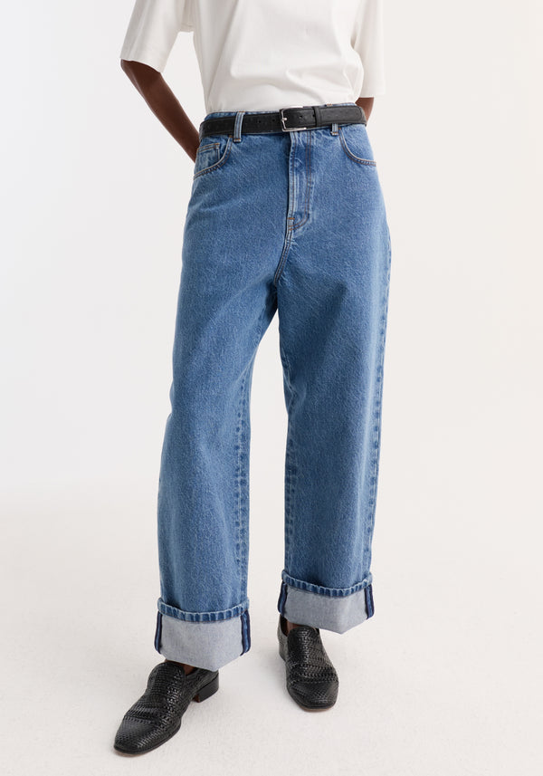 Turn-up baggy denim in heritage blue with wide, rolled-up cuffs and a low-waist fit, styled with a tucked-in white T-shirt and black loafers.