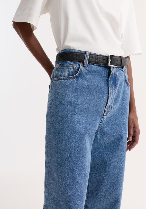 Person wearing Turn-up baggy denim | heritage blue, featuring a low-rise, wide-leg fit and turned-up hems, paired with a black leather belt.