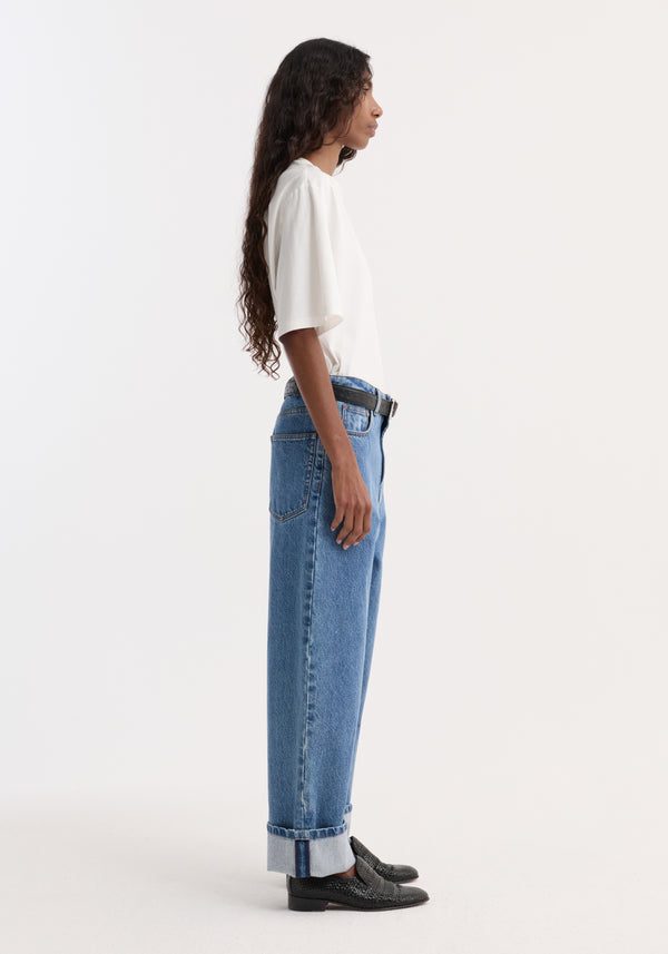 A young woman models Turn-up baggy denim in heritage blue, showcasing a low-waist, wide-leg fit with rolled cuffs and a black belt.