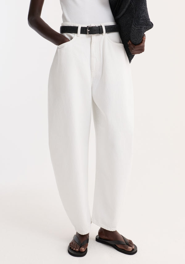Lower half of a person wearing Sculptural denim trousers | optic white, with a high waist and balloon leg, styled with a black belt and sandals.