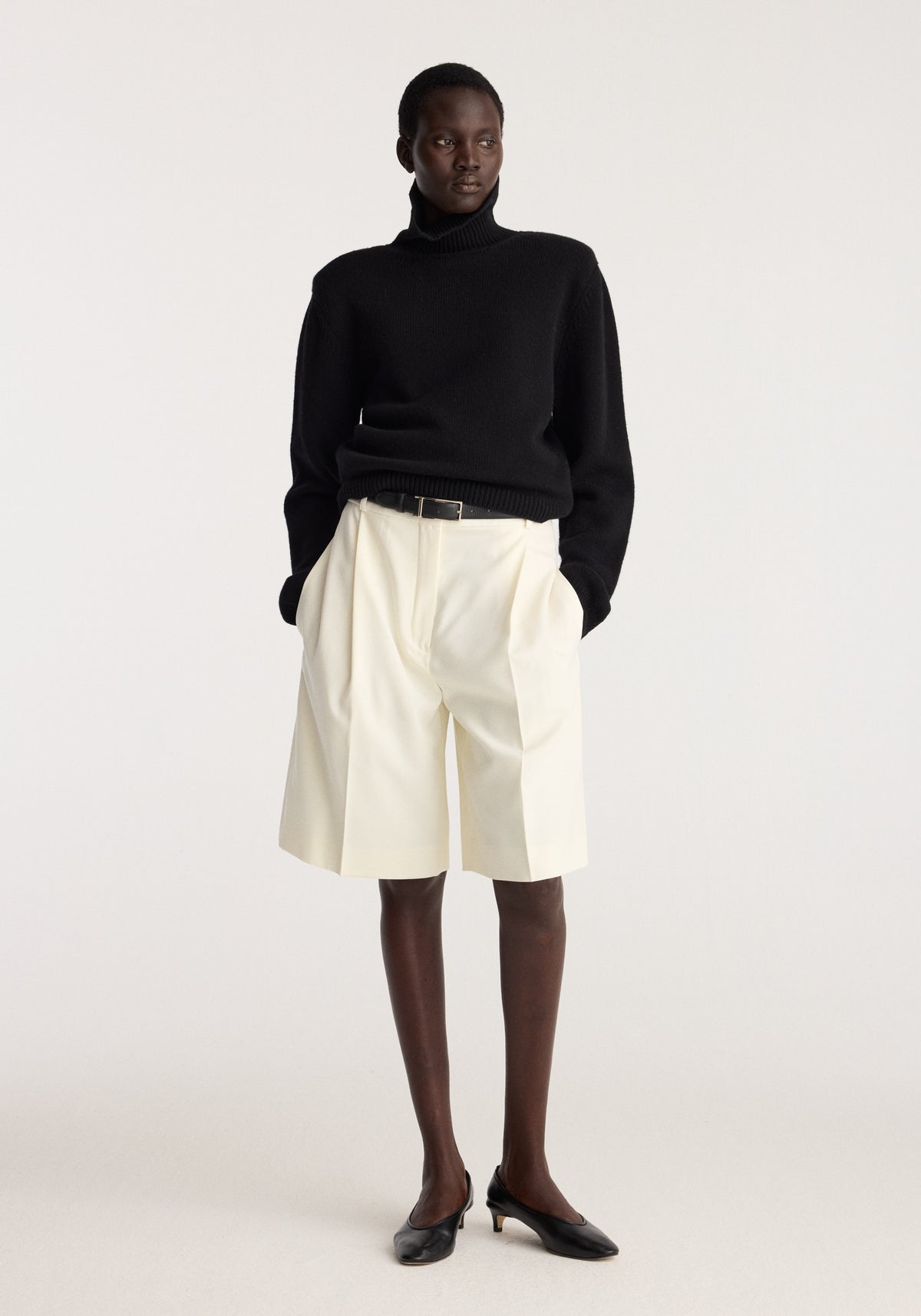 Tailored single pleat shorts | off white worn with a black turtleneck and black shoes on a model in a studio setting