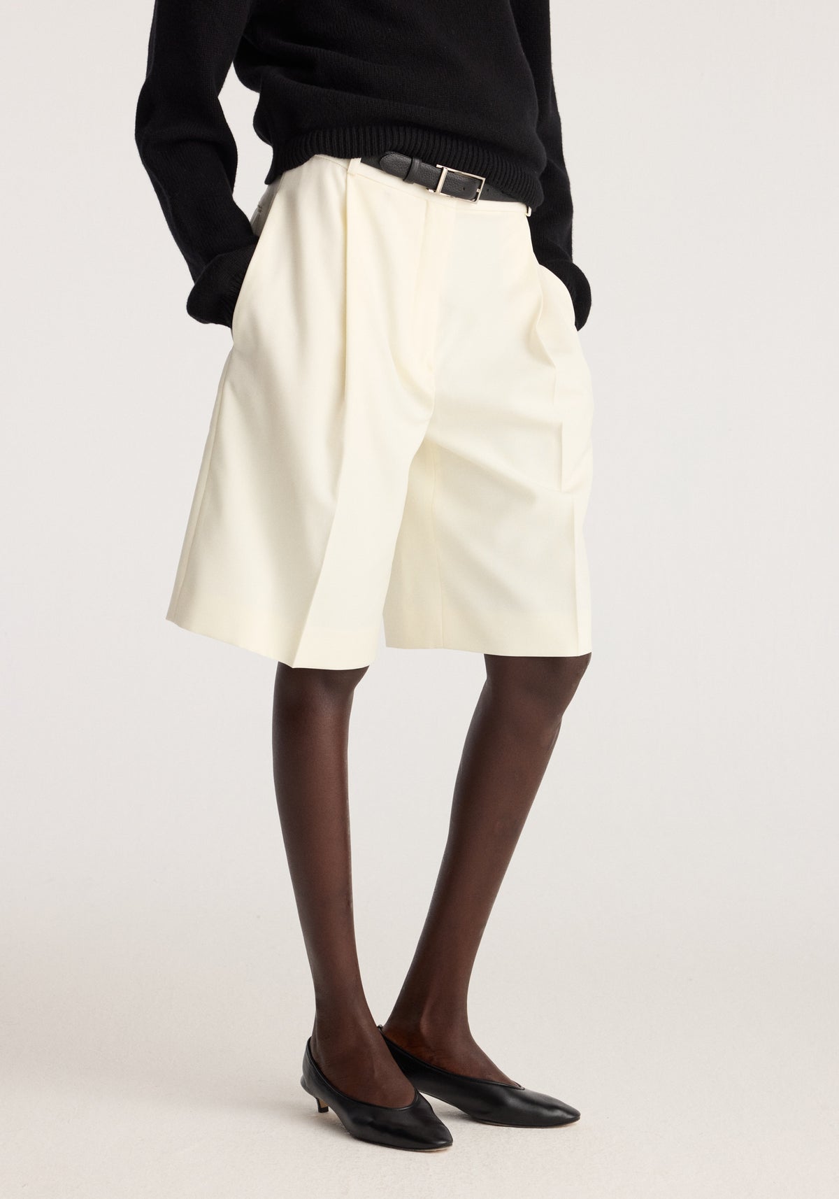 Tailored single pleat shorts | off white worn with a black sweater and black flats showing the relaxed fit and single front pleat on a model