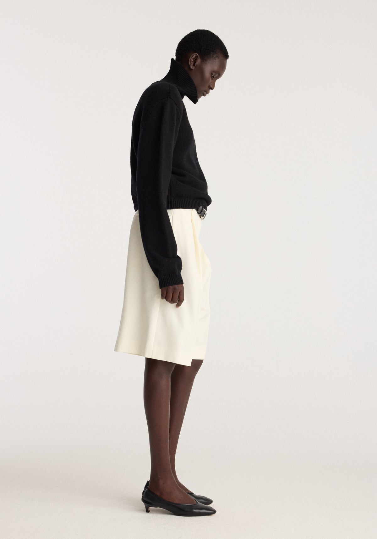 Tailored single pleat shorts | off white shown on a model in side profile with a black sweater and black flats against a light studio background