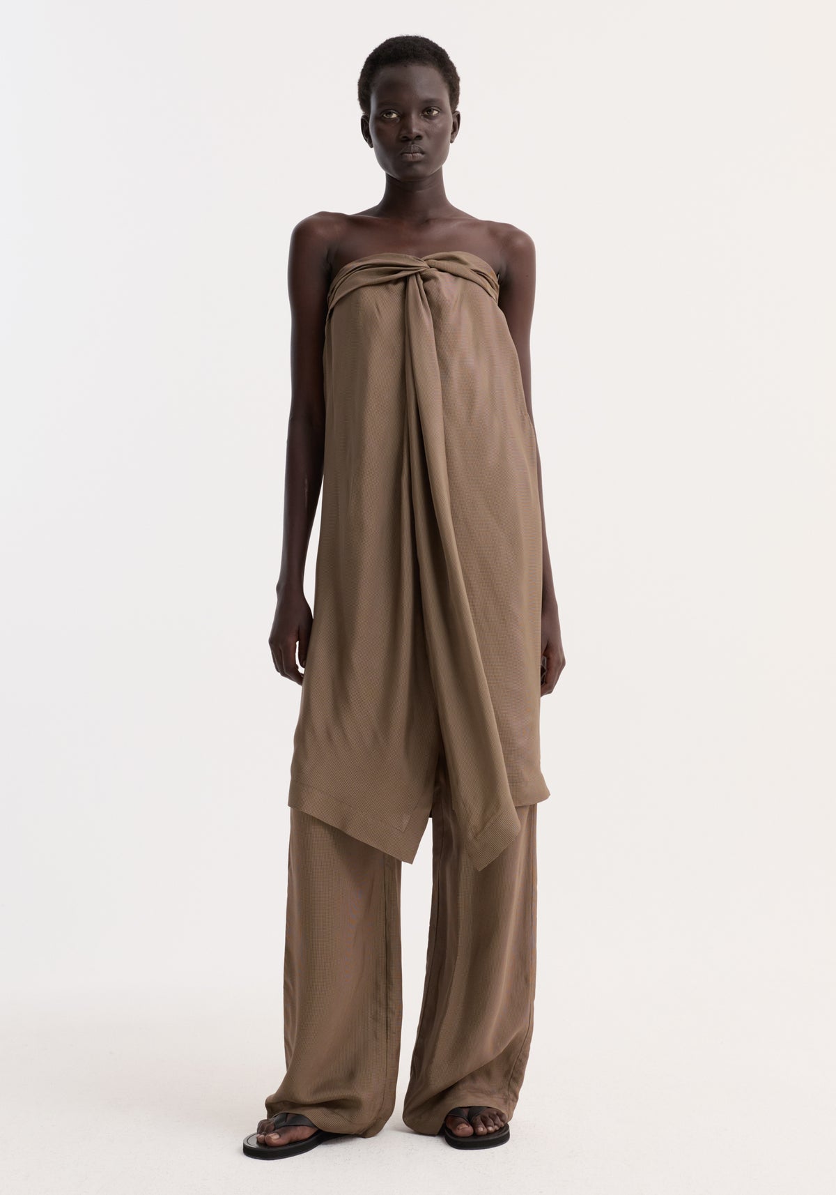 Model in Sarong top with front slit and knot detail, wearing matching wide-leg trousers and black sandals, showcasing a minimal, editorial look.