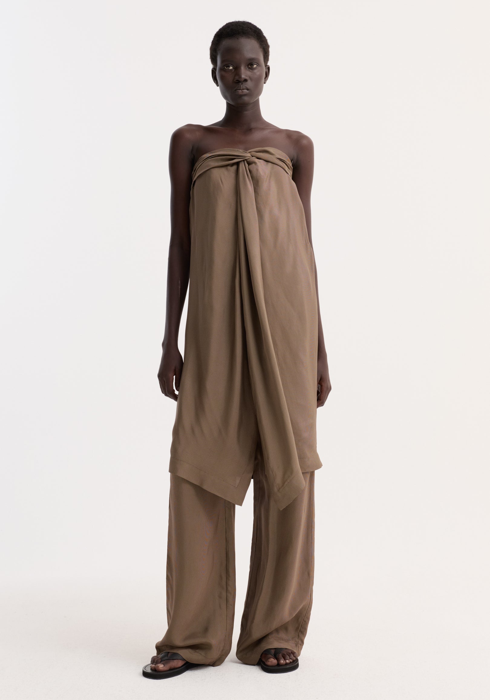Model in Sarong top with front slit and knot detail, wearing matching wide-leg trousers and black sandals, showcasing a minimal, editorial look.