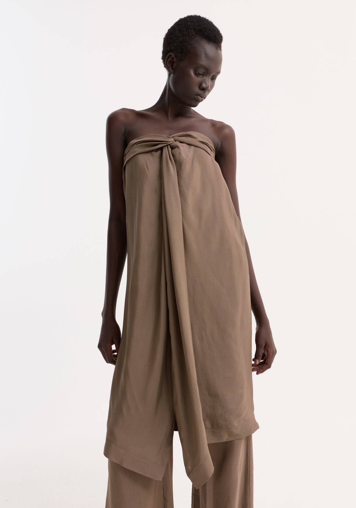 Model in Sarong top | brown mini check, featuring a sarong-style knot, fluid front slit, and integrated bustier, paired with wide-leg pants.