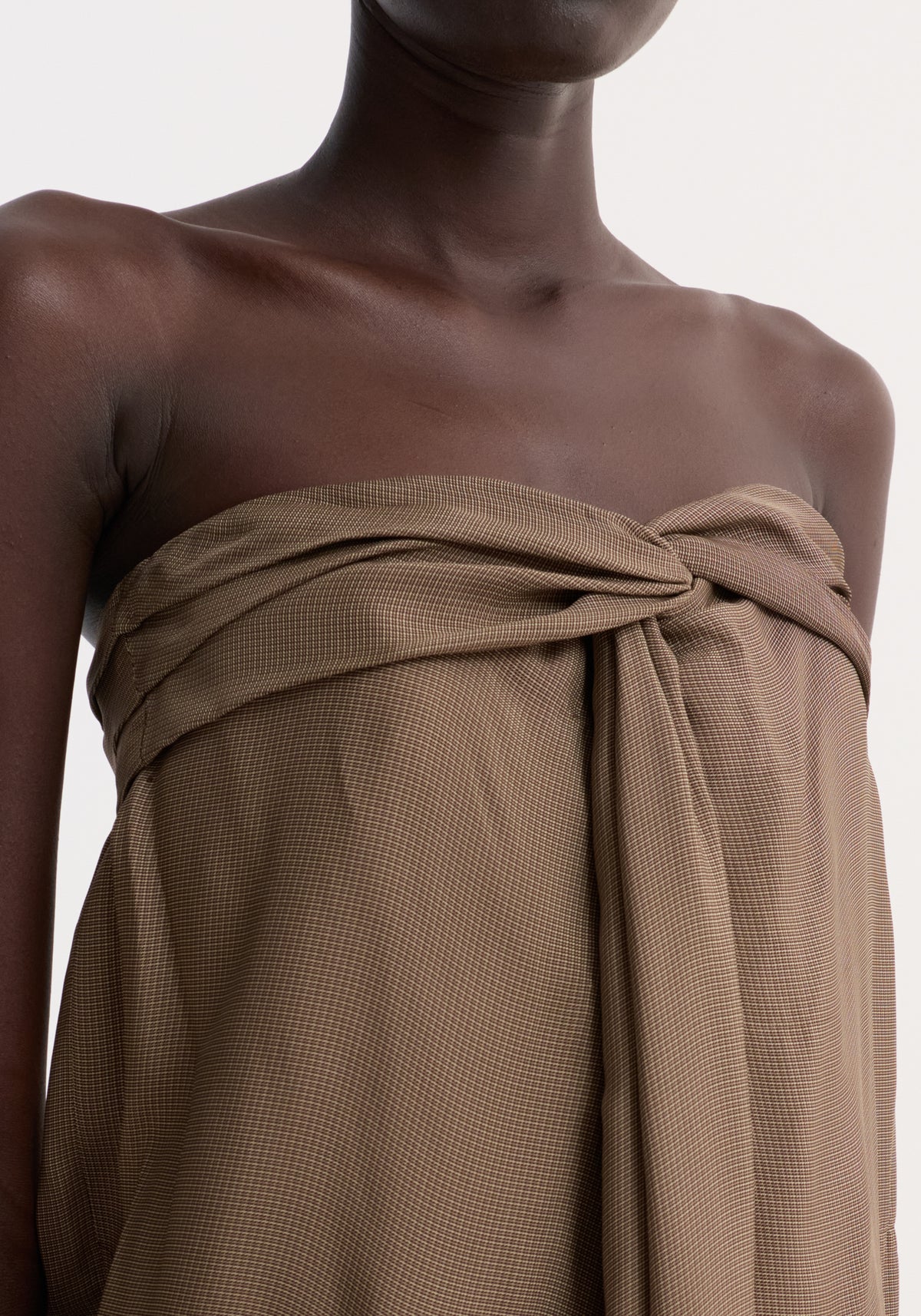 Close-up of a model wearing the Sarong top | brown mini check, featuring a twist knot at the bust and a fluid front slit with inner bustier.