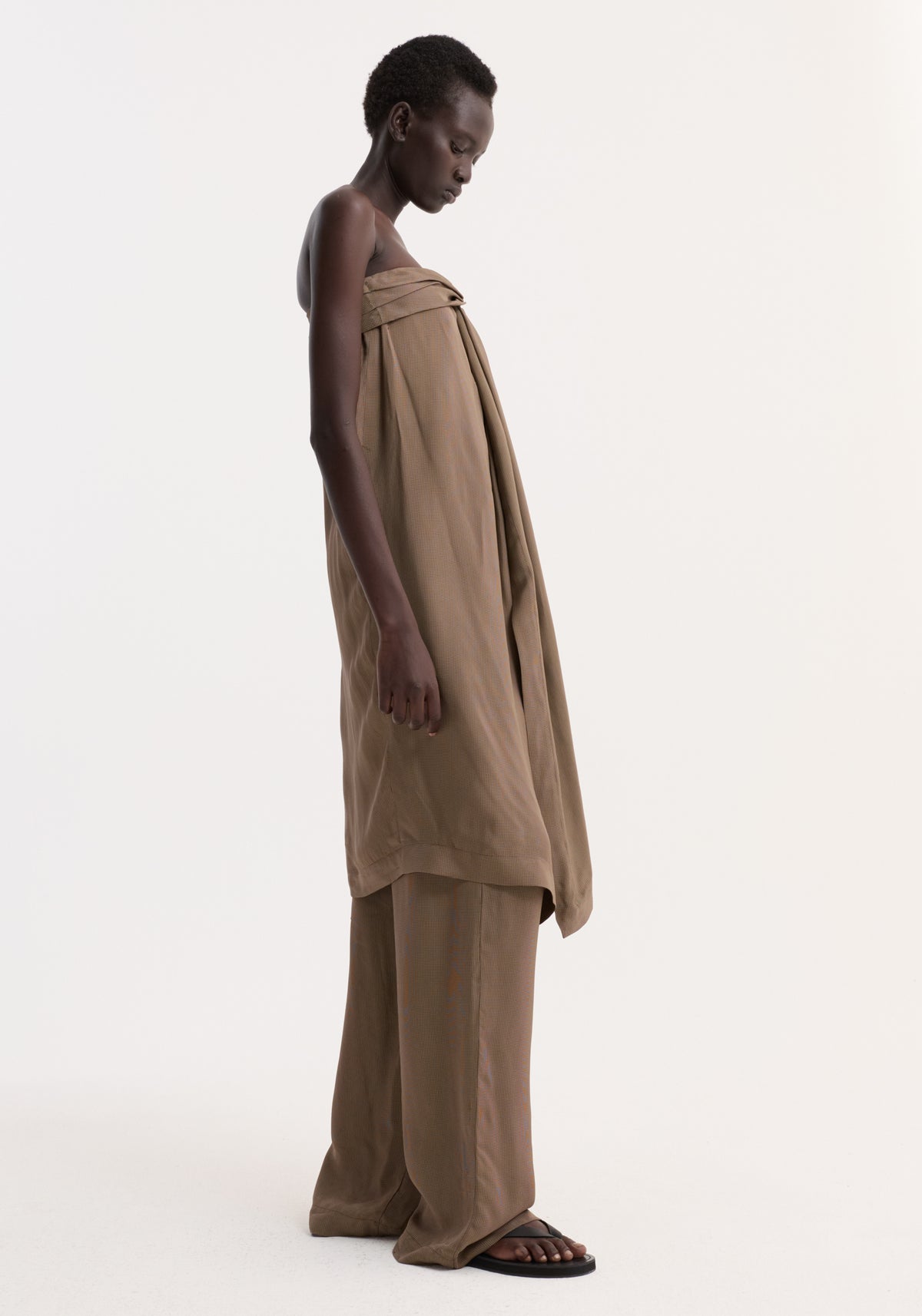 Model in profile wearing Sarong top | brown mini check, featuring a front knot, slit, and integrated bustier. Paired with matching trousers and black sandals.