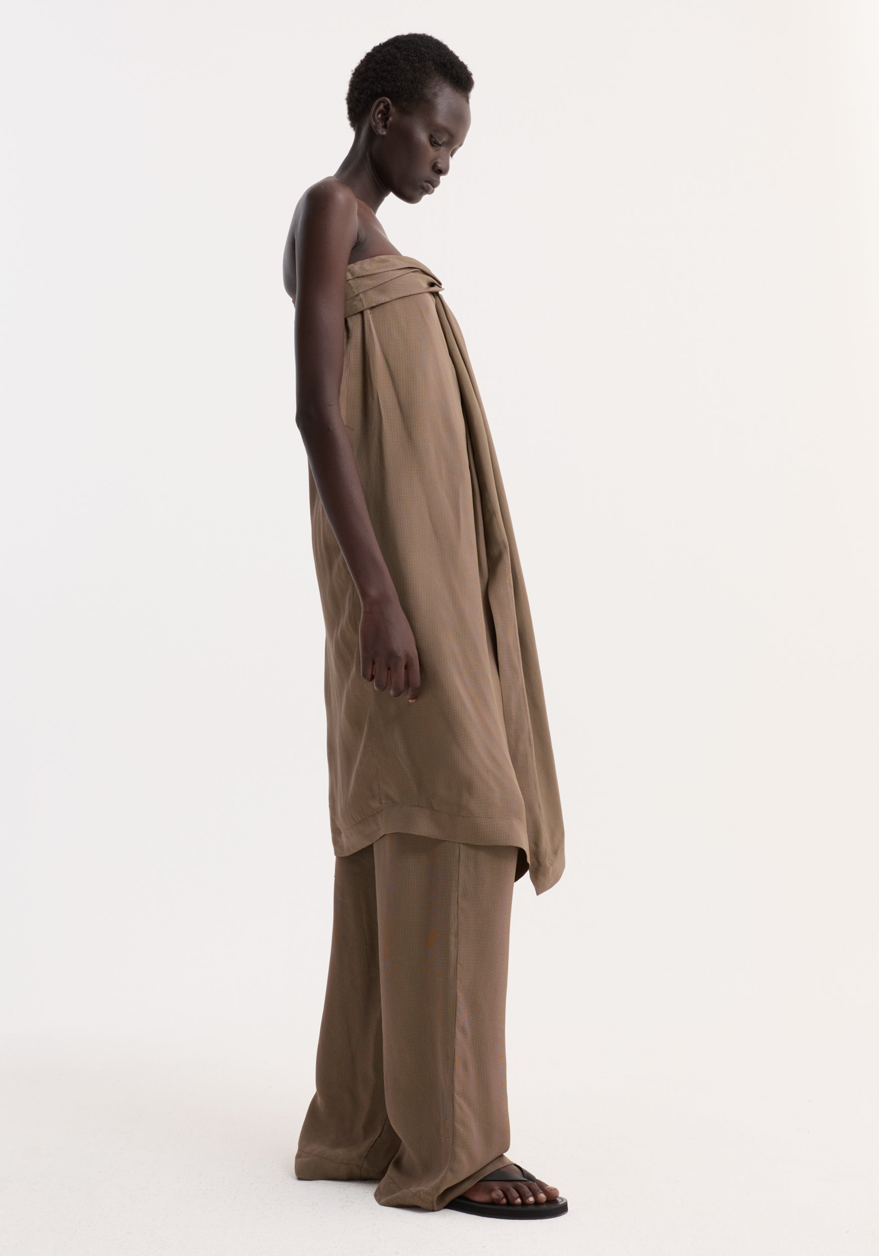 Model in profile wearing Sarong top | brown mini check, featuring a front knot, slit, and integrated bustier. Paired with matching trousers and black sandals.