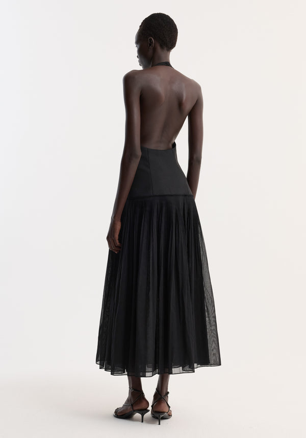 Pleated muslin halter dress | black, showcasing a backless design with a structured bodice and flowing pleated skirt, worn by a model in strappy heels.