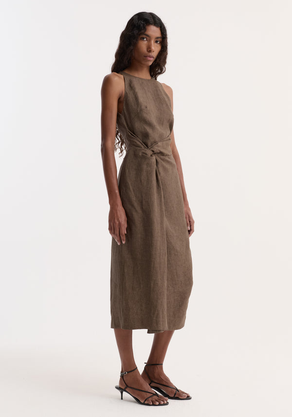 Model in Sarong dress | brown melange, calf-length linen with a high neckline, and waist twist detail, paired with black strappy kitten-heel sandals.