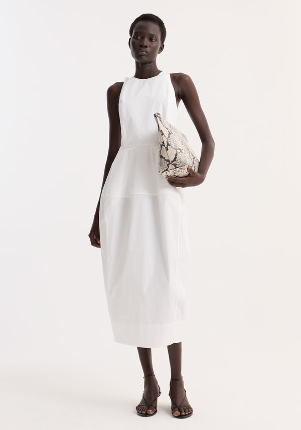 Model in sculptural poplin dress, optic white, with a sleeveless design, fitted waist, and trapezium-shaped skirt, holding a snakeskin-print clutch.
