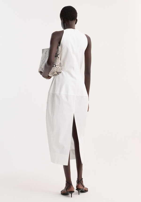 Individual in a Sculptural poplin dress | optic white, showcasing a fitted waist and trapezium-shaped skirt with back slit, holding a gray snakeskin tote.