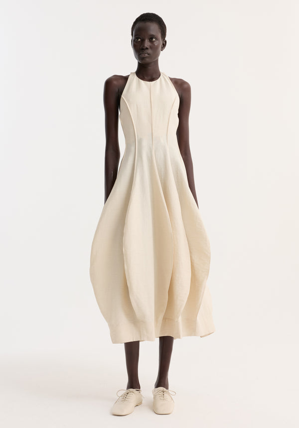Tall model in Open Back Tulip Dress | Butter, featuring a fitted bodice, balloon skirt, halter neck, and lace-up flats against a plain background.