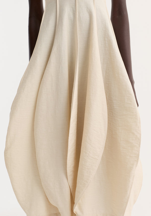 Open back tulip dress in butter, featuring a halter neck and balloon-shaped skirt with seam detailing, worn by a dark-skinned model highlighting its elegant, sculptural silhouette.