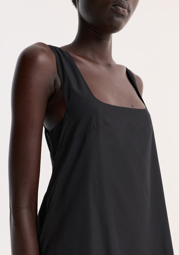 Technical volume dress in black on model, showcasing sleeveless design, scooped square neckline, and part of balloon hemline against a light background.