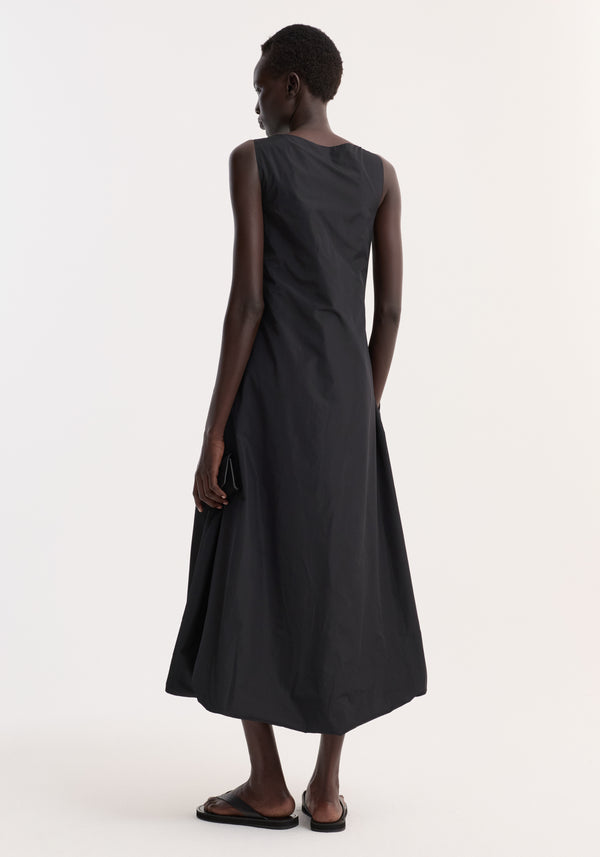 Technical volume dress | black worn by a person, features a sleeveless design, scooped square neckline, balloon hemline, and wide straps, accessorized with a small wallet.