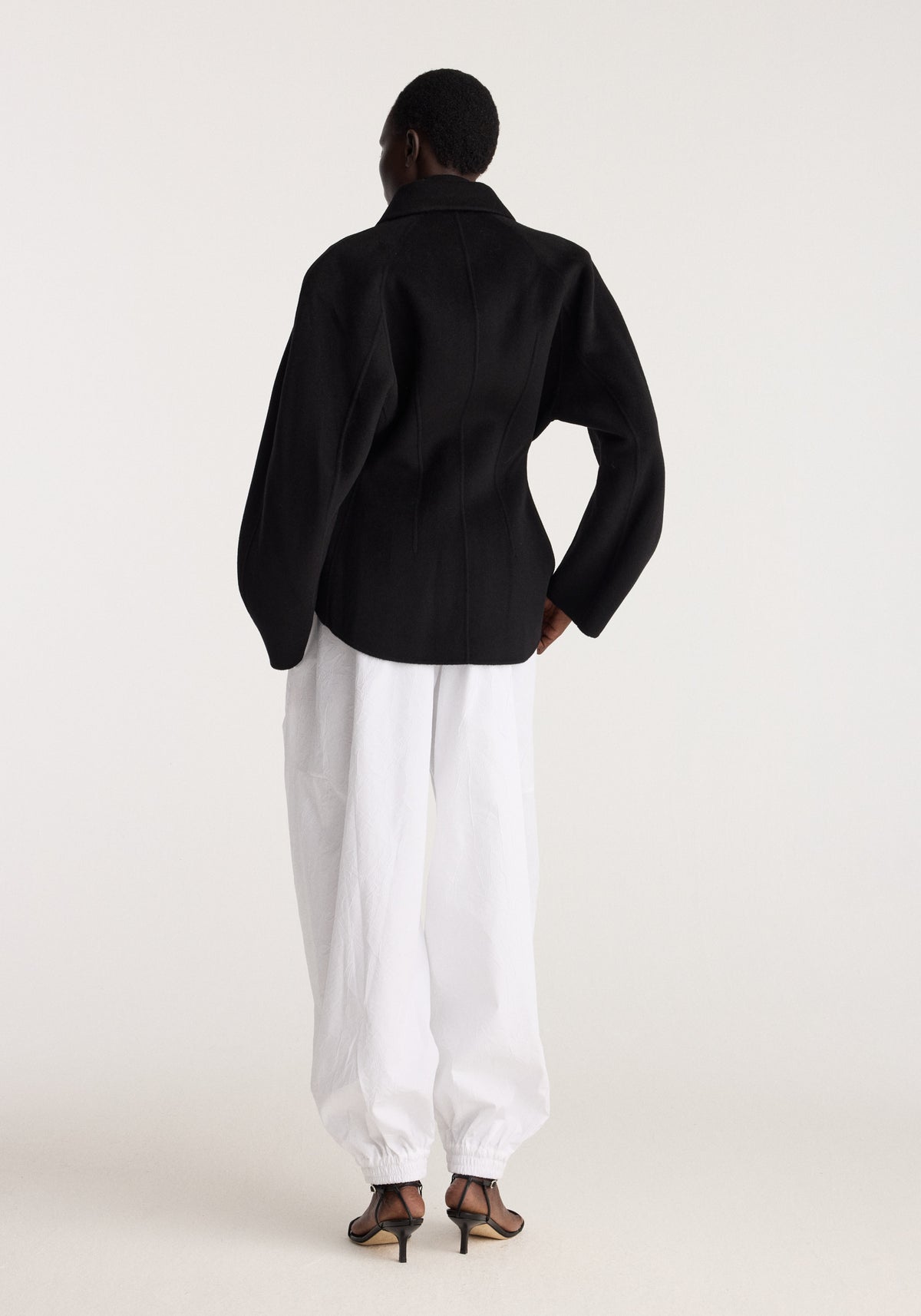 Double-faced sculptural jacket | black shown from the back on a model, featuring a structured silhouette, raised collar, curved sleeves, and tailored black finish.