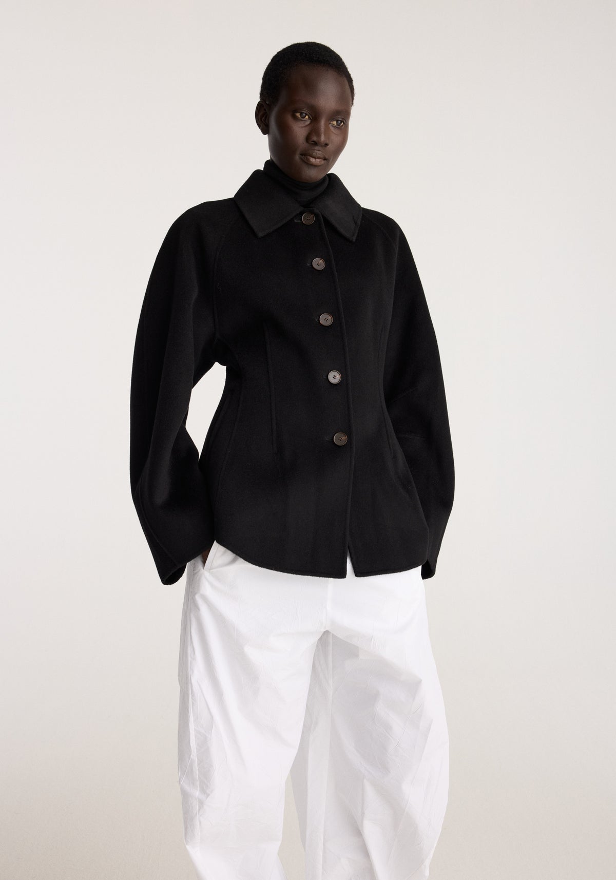 Double-faced sculptural jacket | black worn by a model with a pointed collar button front and sculpted sleeves paired with loose white trousers
