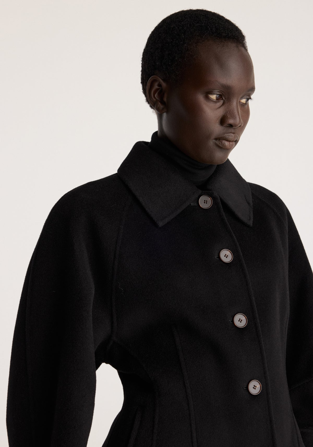 Double-faced sculptural jacket | black worn by a model, featuring a high collar, oversized lapels, sculpted waist, long sleeves, and front buttons