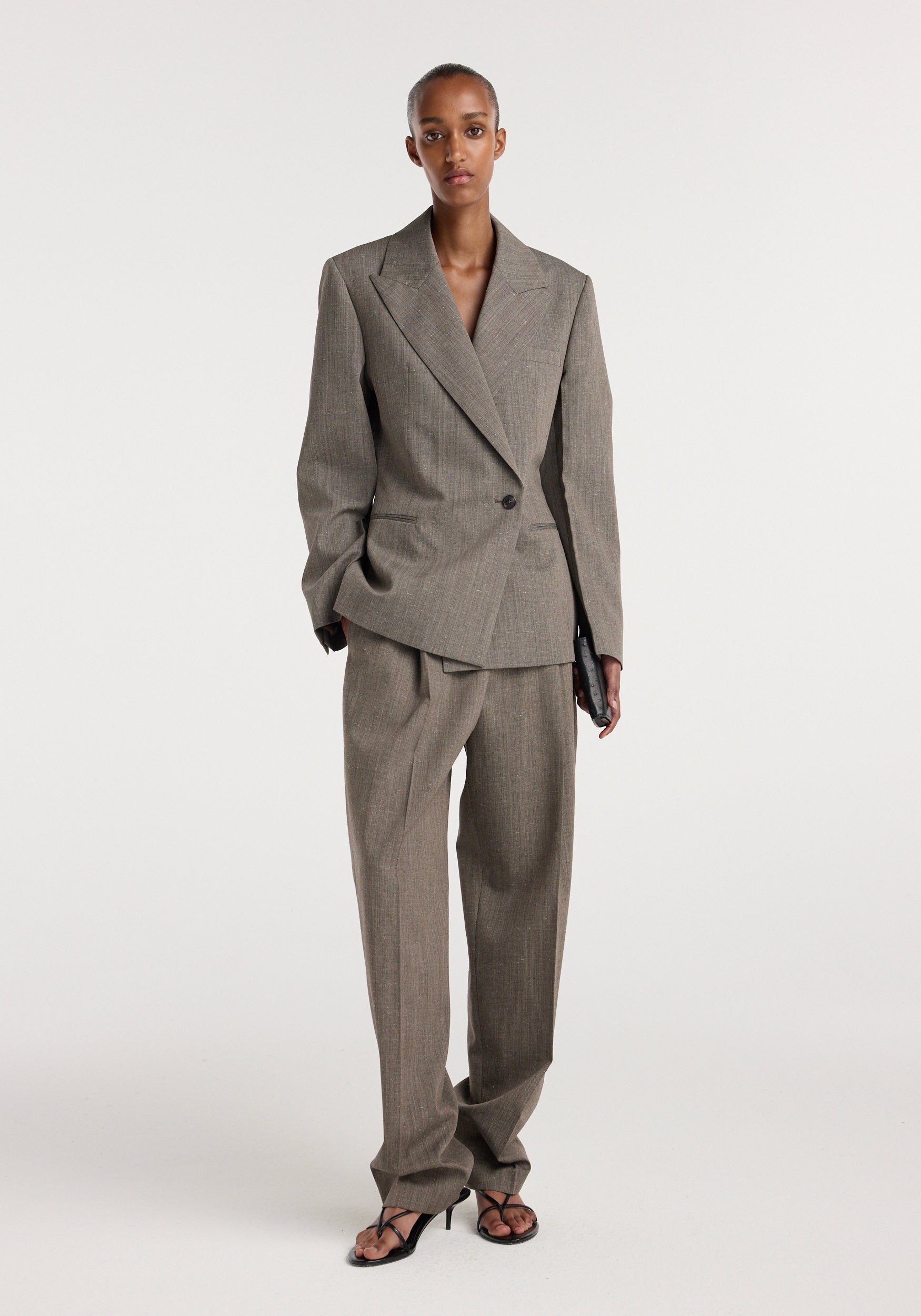 Model wearing an hourglass shaped blazer | earth slub in a neutral brown tone with matching wide-leg trousers and black strappy heels against a plain white background.