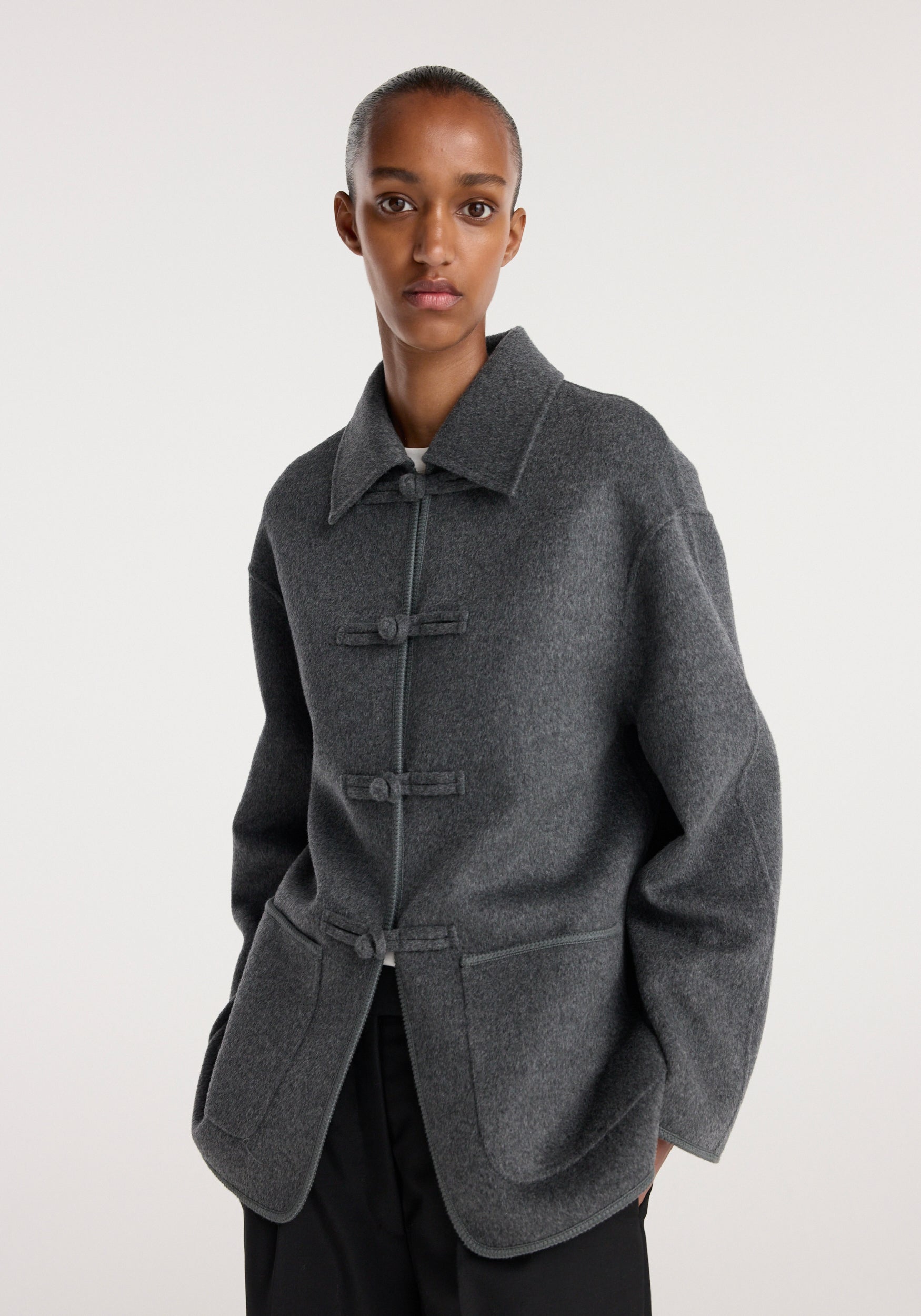 Model wearing a dark grey melange Double-faced wool pankou closure jacket with three pankou closures, a wide collar, and large front patch pockets.
