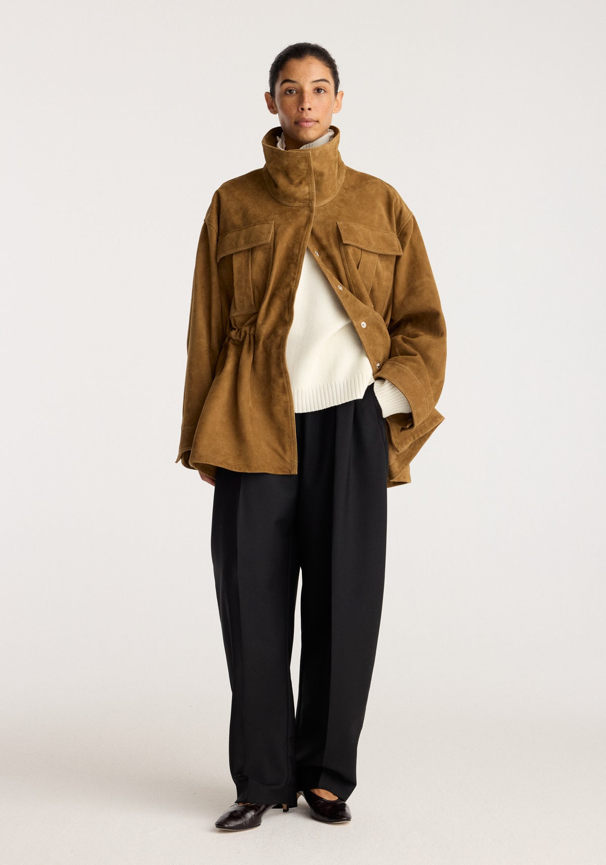 Sculptural suede jacket | sage worn by a model with a high collar front pockets button closure and relaxed sculptural fit over a cream knit sweater