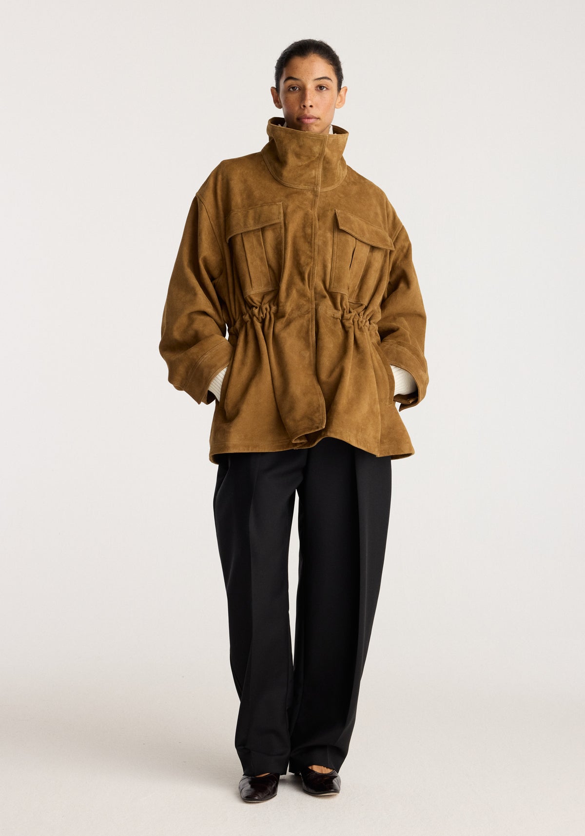 Sculptural suede jacket | sage shown on a model with a high collar patch pockets gathered waist and relaxed sleeves styled with black trousers and shoes