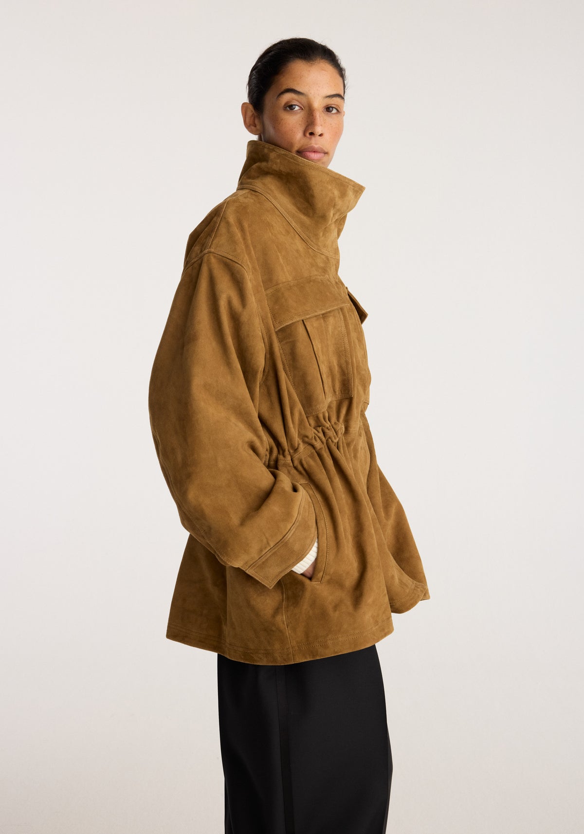 Sculptural suede jacket | sage shown on a model in side profile with a high collar, gathered waist, oversized sleeves, and front pockets