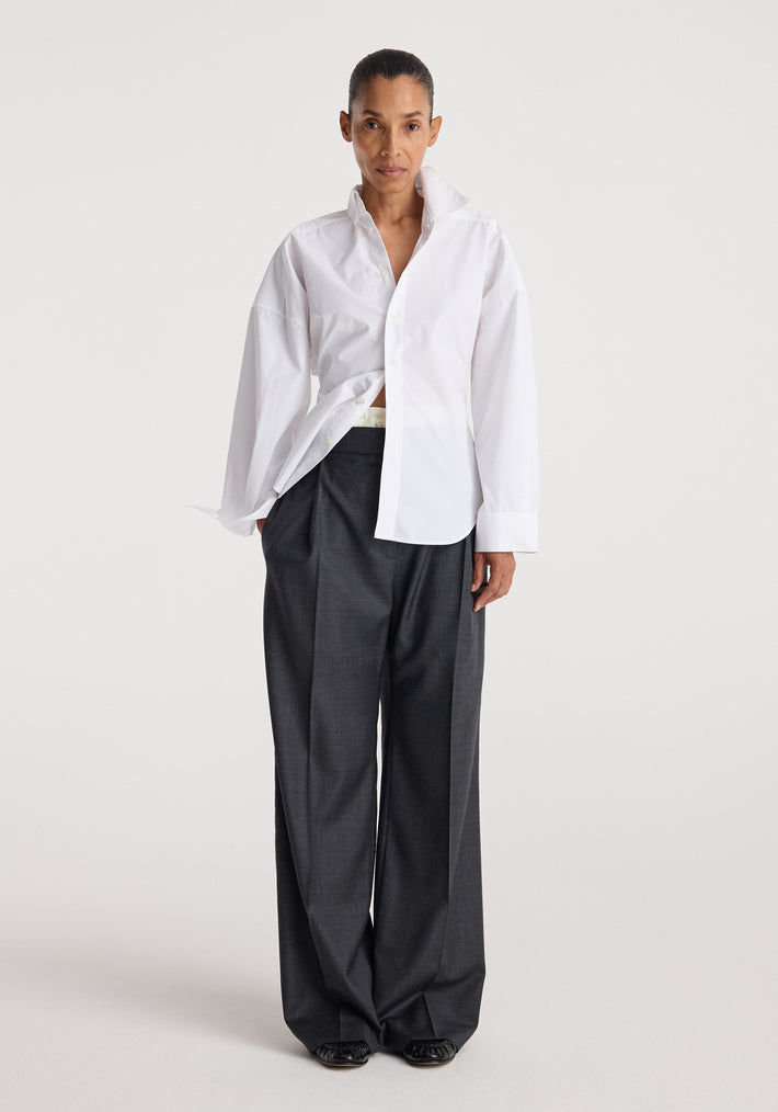 Model wearing a long-sleeve Poplin uneven collar shirt | optic white with a partially open front, paired with loose dark gray pants against a plain background.