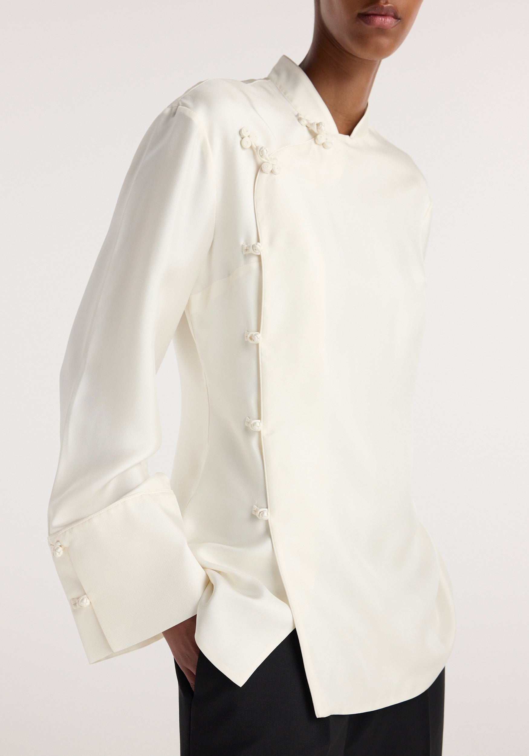 Model wearing a cream Pankou closure silk top | cream featuring asymmetrical front with traditional Chinese button knots, long sleeves with wide cuffs, and a smooth satin finish.