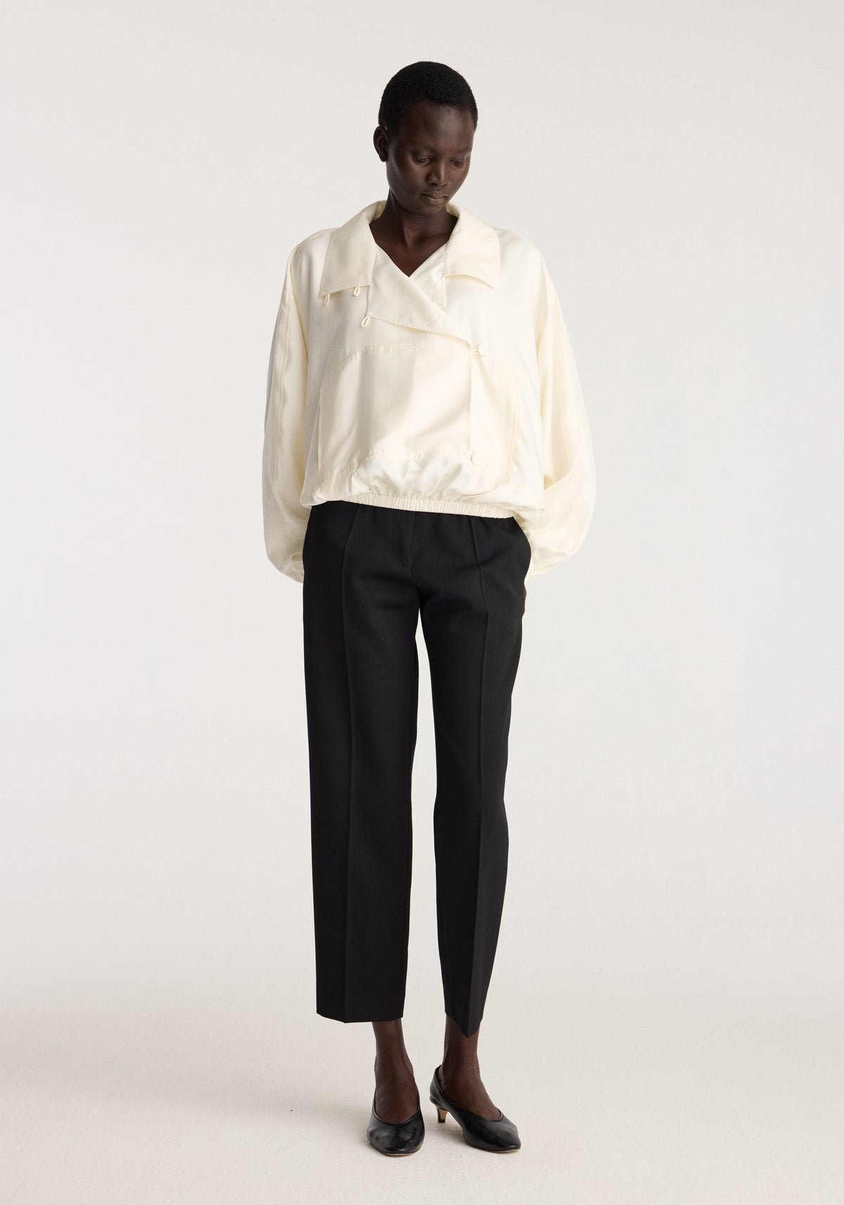 Silk blouson anorak | cream worn by a model with black trousers and black shoes against a light studio background