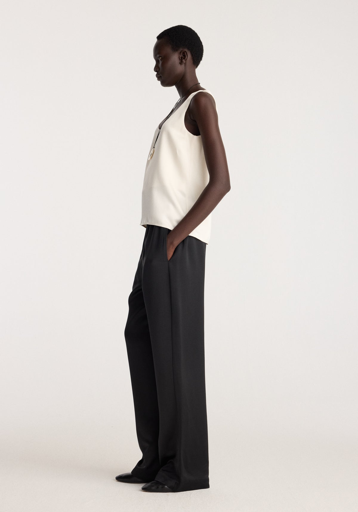 Satin scoop-neck top | ivory worn by a model with black wide-leg trousers in a side-profile studio portrait