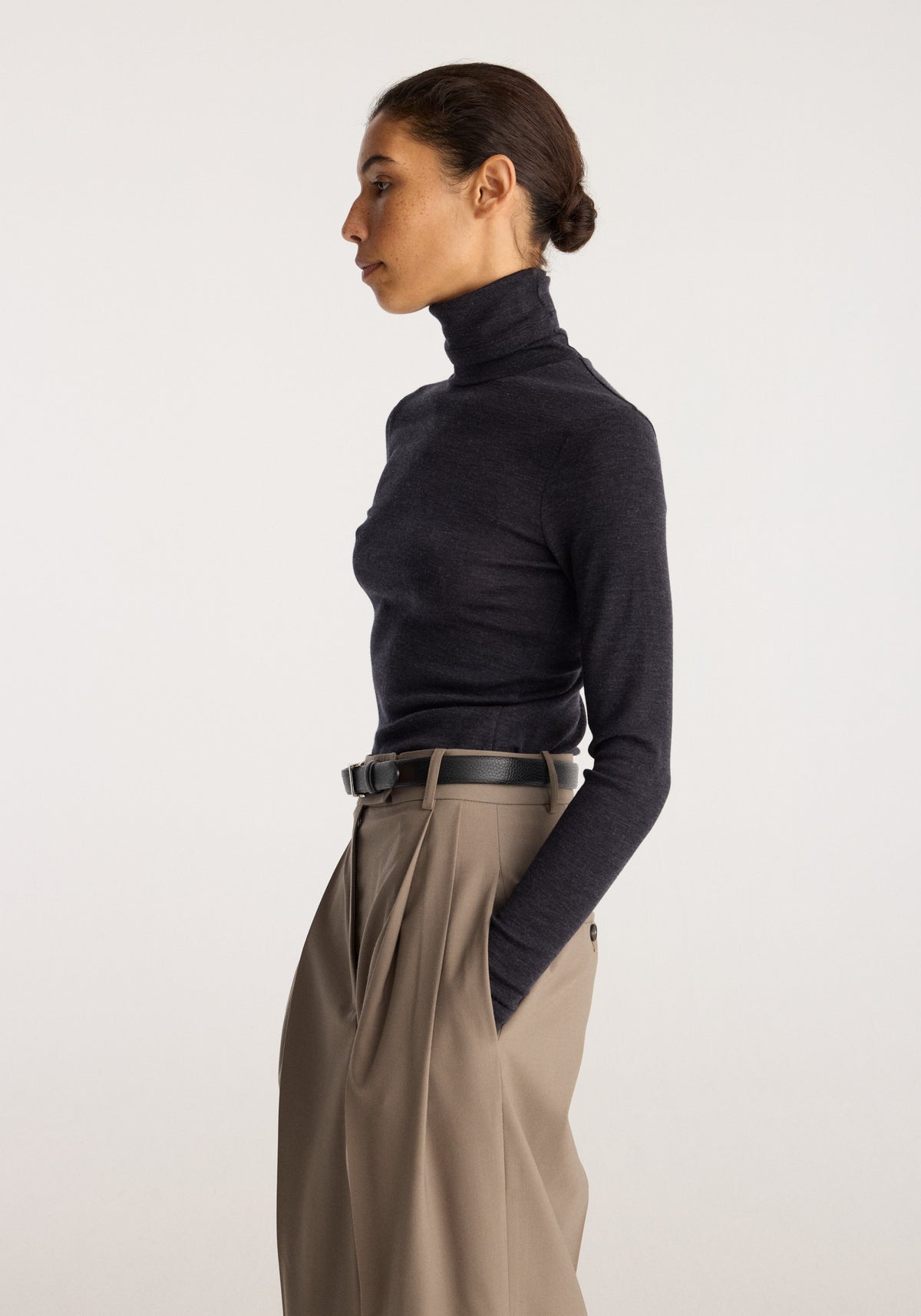 Fine merino turtleneck | anthracite melange worn by a model with tailored taupe trousers in a side profile view