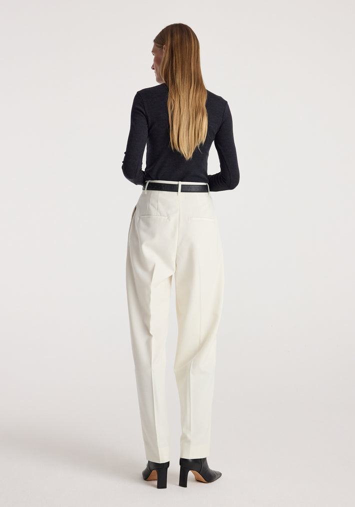 Woman seen from behind wearing a Fine merino turtleneck | anthracite melange paired with white trousers and black heeled ankle boots, standing against a plain background.