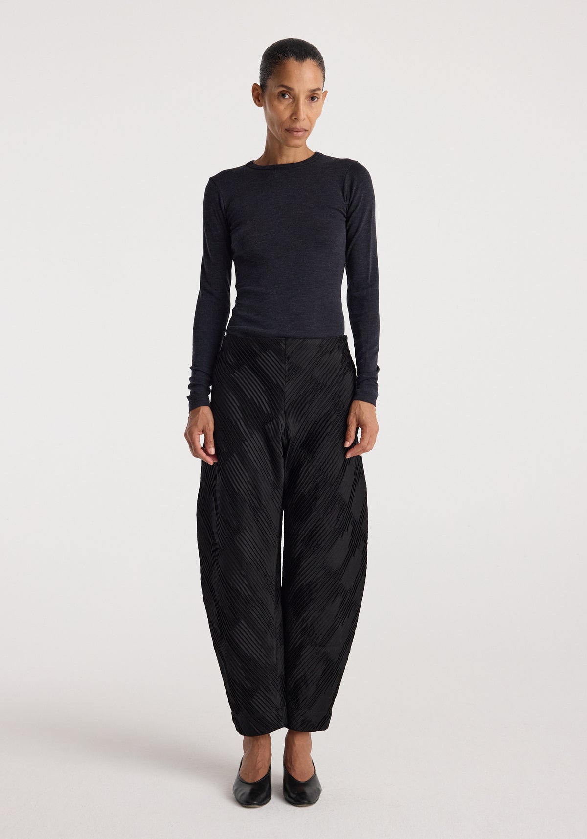 Woman wearing a fitted dark grey long sleeve top paired with loose black textured pants and black heels, showcasing the Fine merino long sleeve | anthracite melange.