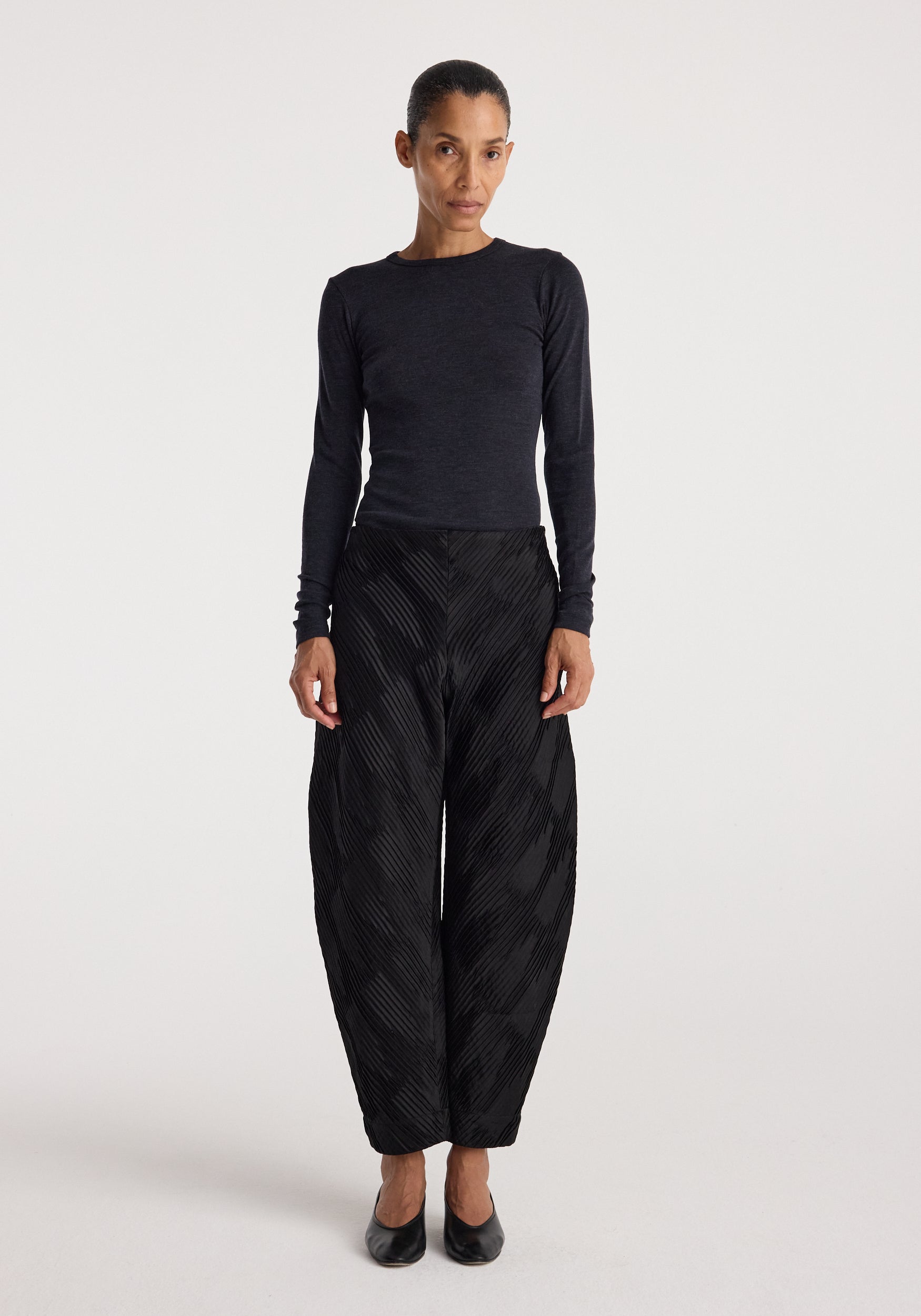 Woman wearing a fitted dark grey long sleeve top paired with loose black textured pants and black heels, showcasing the Fine merino long sleeve | anthracite melange.