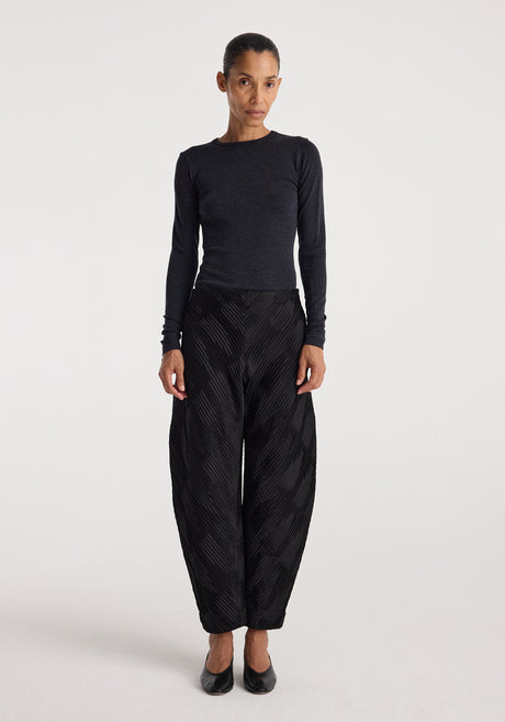 Woman wearing a fitted dark grey long sleeve top paired with loose black textured pants and black heels, showcasing the Fine merino long sleeve | anthracite melange.