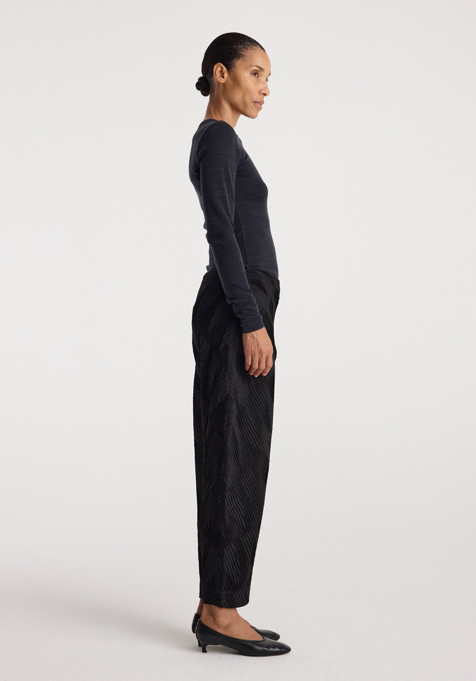 Side profile of a woman wearing a dark fitted long sleeve top paired with black textured pants and black low-heeled shoes, showcasing the Fine merino long sleeve | anthracite melange.