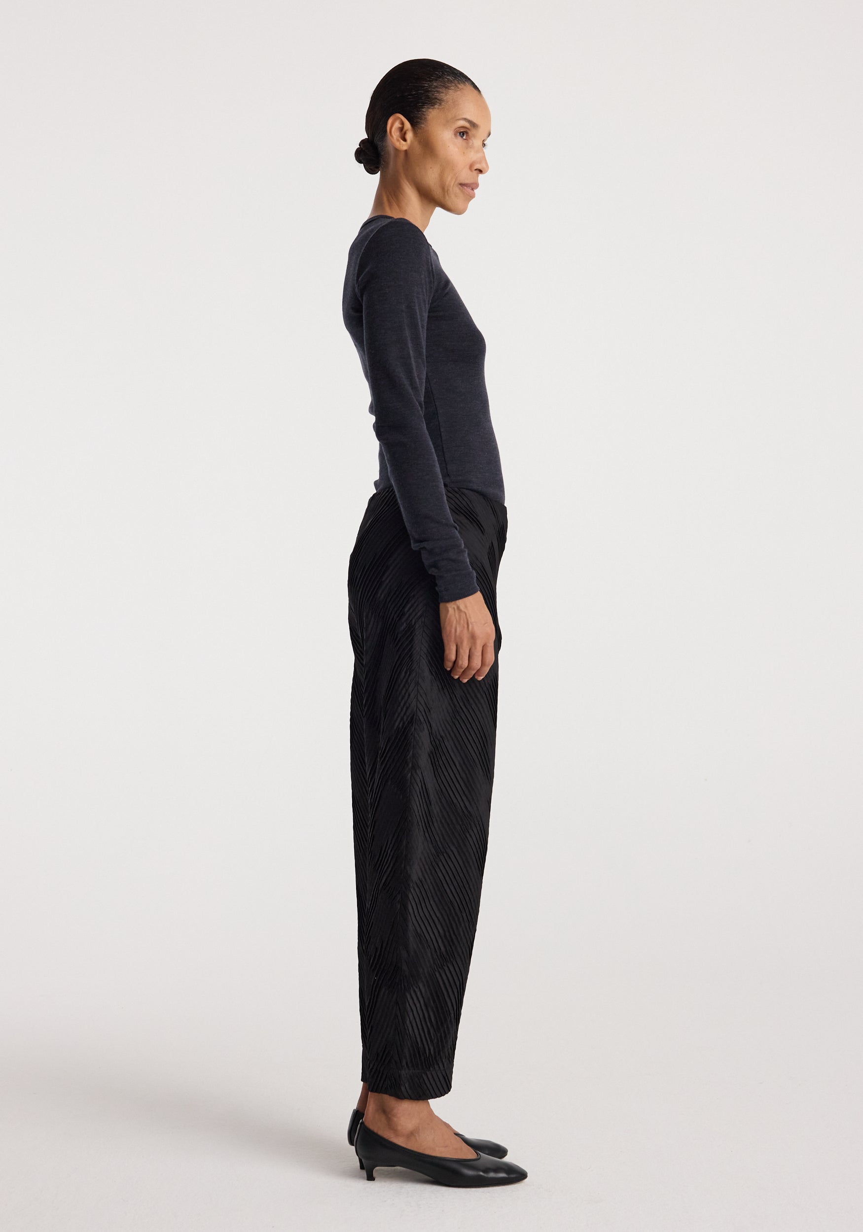 Side profile of a woman wearing a dark fitted long sleeve top paired with black textured pants and black low-heeled shoes, showcasing the Fine merino long sleeve | anthracite melange.