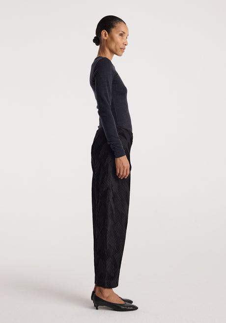 Woman wearing a fitted dark grey long sleeve top paired with loose black textured pants and black heels, showcasing the Fine merino long sleeve | anthracite melange.
