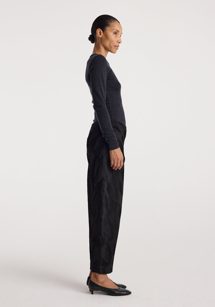 Woman wearing a fitted dark grey long sleeve top paired with loose black textured pants and black heels, showcasing the Fine merino long sleeve | anthracite melange.