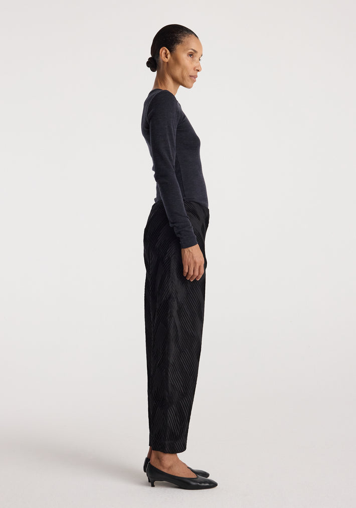 Side profile of a woman wearing a dark fitted long sleeve top paired with black textured pants and black low-heeled shoes, showcasing the Fine merino long sleeve | anthracite melange.
