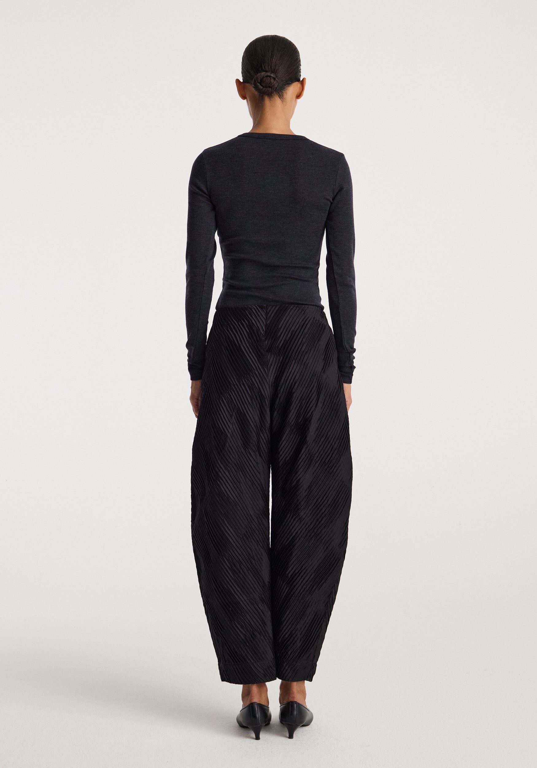 Woman shown from behind wearing a Fine merino long sleeve | anthracite melange paired with wide-leg textured black pants and black heels against a plain light background.