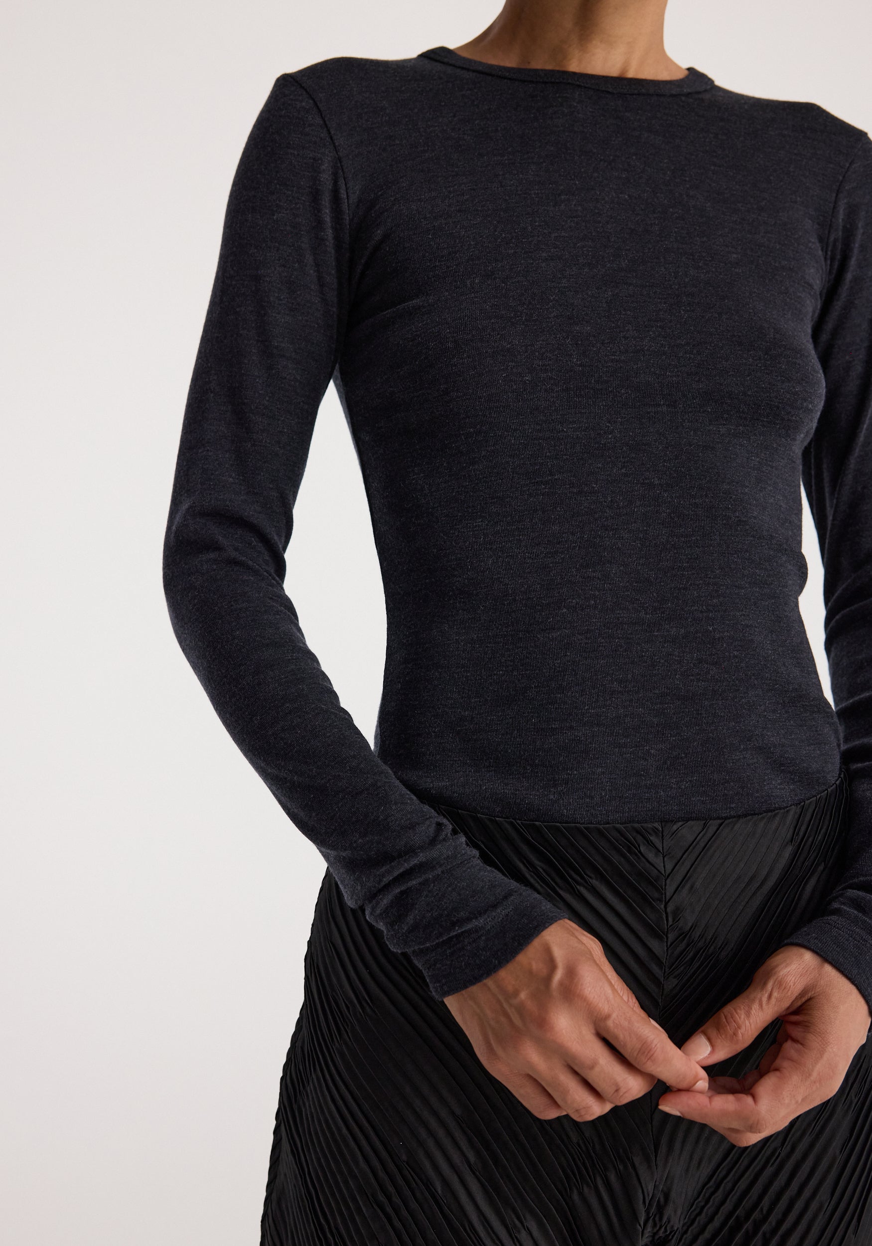 Close-up of a person wearing a fine merino long sleeve | anthracite melange, featuring a fitted, textured dark grey top with long sleeves and a round neckline.