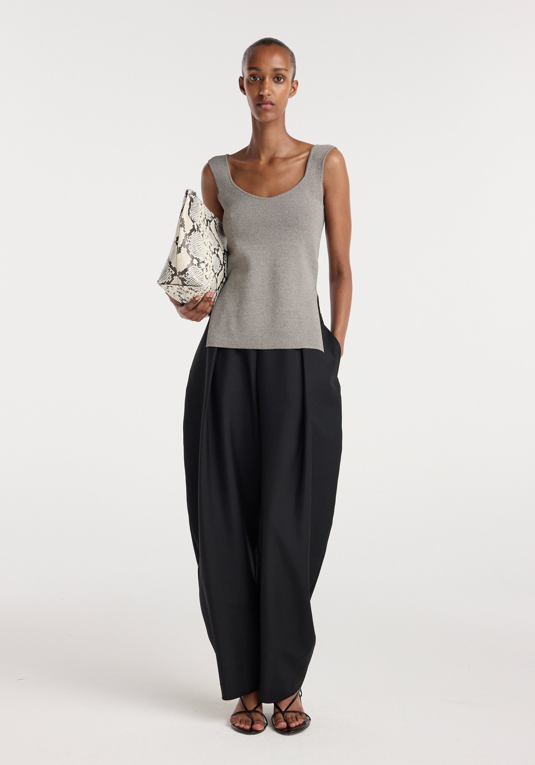Woman wearing a taupe melange Long knitted bustier top paired with black wide-leg trousers, holding a snake-print handbag, and black strappy sandals against a plain white background.