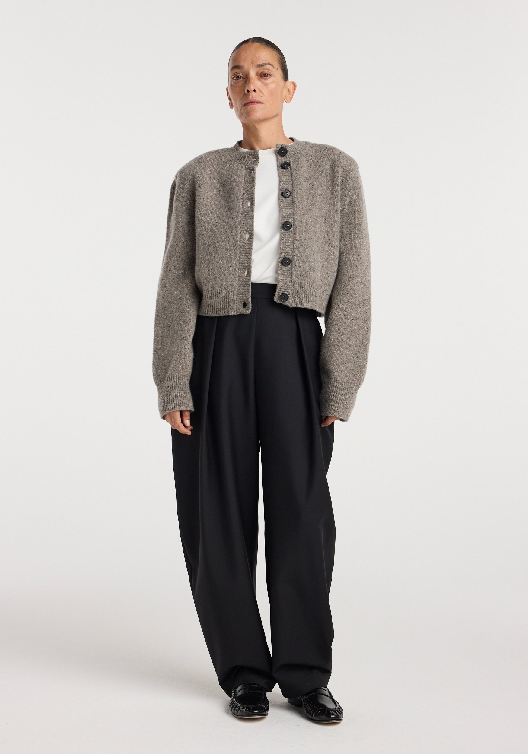 Woman wearing a Statement mouliné cardigan | dark taupe melange with button closure, paired with black wide-leg trousers and black shoes against a plain background.